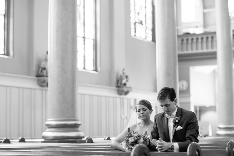 Black and white image of a bride and groom kneeling in prayer.