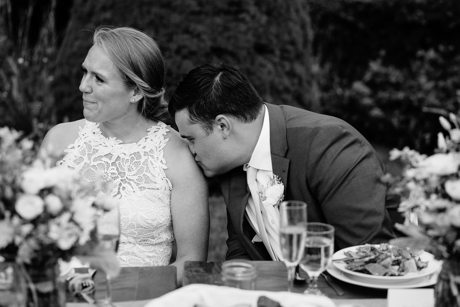 groom tenderly kisses brides shoulder during wedding reception