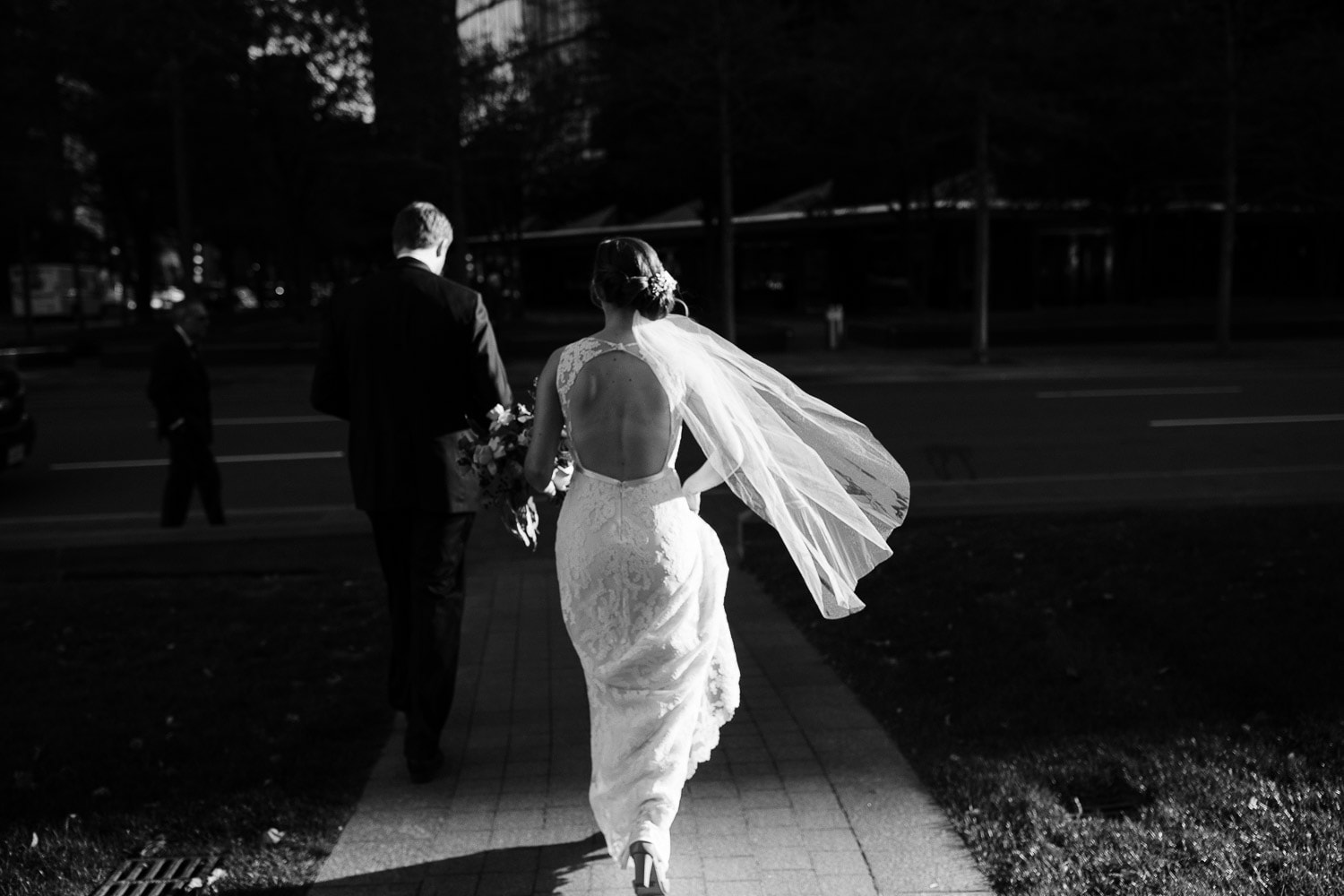 black and white image of a bride and groom walking away from Trinity Church Boston, illuminated by a sliver of light